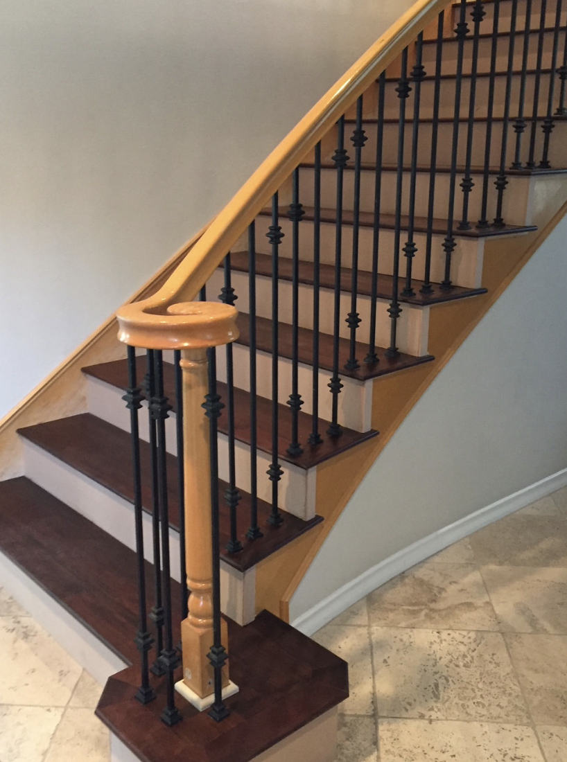 Curved wooden staircase with black iron balusters and dark wooden steps, next to a tiled floor.